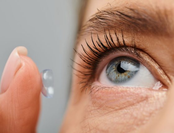 close up of good looking woman wearing attentively her contact lens while posing on gray background